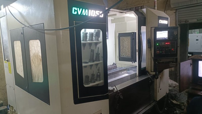 The Cosmos CVM 1050 vertical machining centre, toolholders racked behind the door and a mould plate set up on the table.